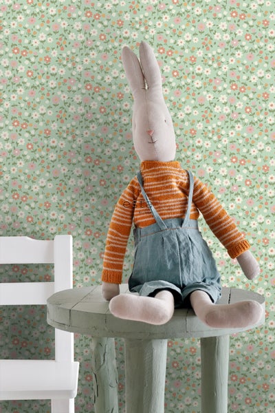 Dekoratives Zimmer mit einer Tapete mit Blumenmuster und einem Stoffhasen auf einem kleinen Tisch