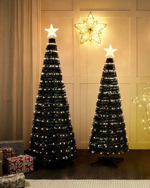 Zwei beleuchtete künstliche Weihnachtsbäume mit Sternspitze in einem Wohnzimmer mit Weihnachtsdekoration.