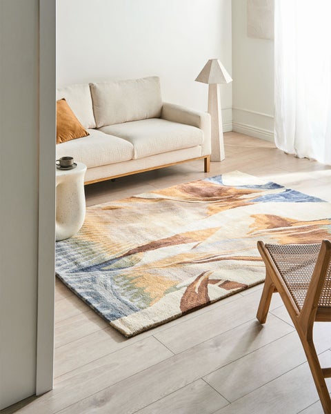 Helles, minimalistisches Wohnzimmer mit einem rechteckigen Teppich mit abstraktem Muster in Beige, Braun und Blau auf hellem Holzboden.