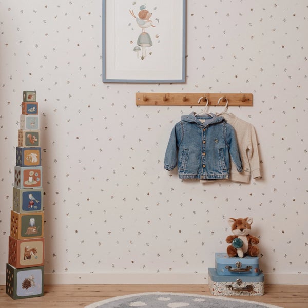 Vliestapete im Kinderzimmer mit feinem Waldmuster aus Pilzen und Blättern, dekoriert mit Holzgarderobe, Stapelsteinen, Spielzeug und Wandbild.