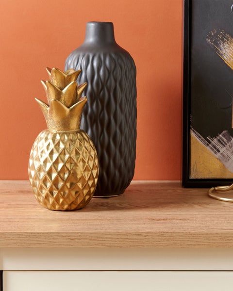 Dekorative goldene Ananas neben einer dunklen Vase als Tischdekoration
