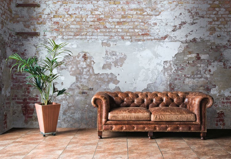 Wohnzimmer mit braunem Ledersofa, Zimmerpflanze im Topf und Ziegelwand