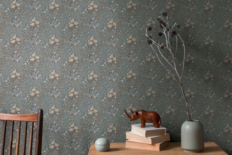 Detailaufnahme einer Wand mit floral gemusterter Tapete, einem Holztisch und dekorativen Gegenständen.