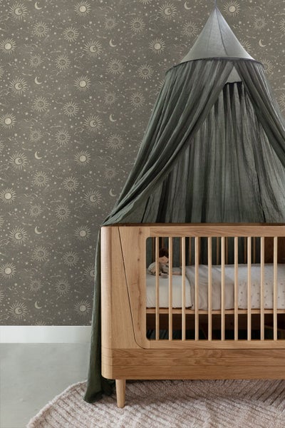 Vliestapete mit Sonnen- und Mondmuster im Kinderzimmer an der Wand hinter einem Babybett aus Holz mit Baldachin.