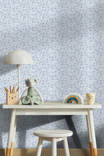 Tapete mit feinem Blumenmuster hinter einem hellen Schreibtisch im Kinderzimmer mit Lampe, Kuscheltier und Holzspielzeug.