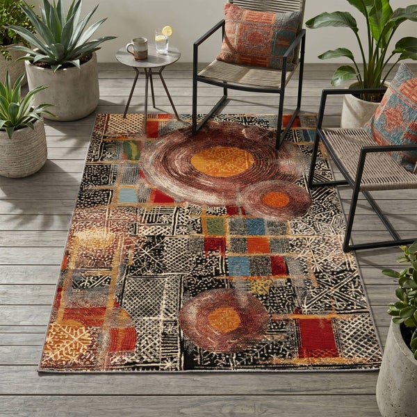 Moderner Außenteppich mit abstraktem Muster auf einer Holzterrasse, umgeben von Gartenmöbeln und Topfpflanzen.