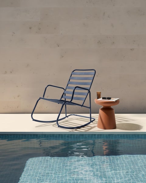 Szene mit einem blauen Schaukelstuhl und einem Beistelltisch neben einem Pool.
