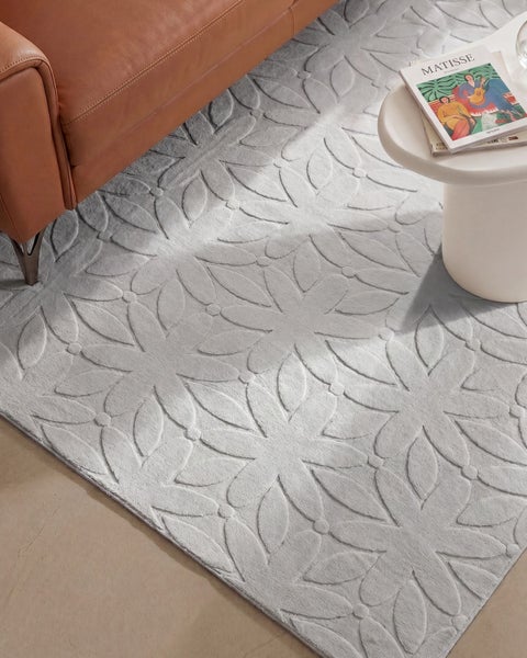 Wohnzimmerteppich mit floralem Prägemuster vor einem Ledersofa und einem Beistelltisch