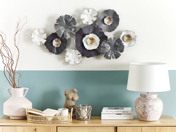 Dekoratives Arrangement mit Metallblumenwanddekoration, Lampe und Accessoires auf einem Holzschrank