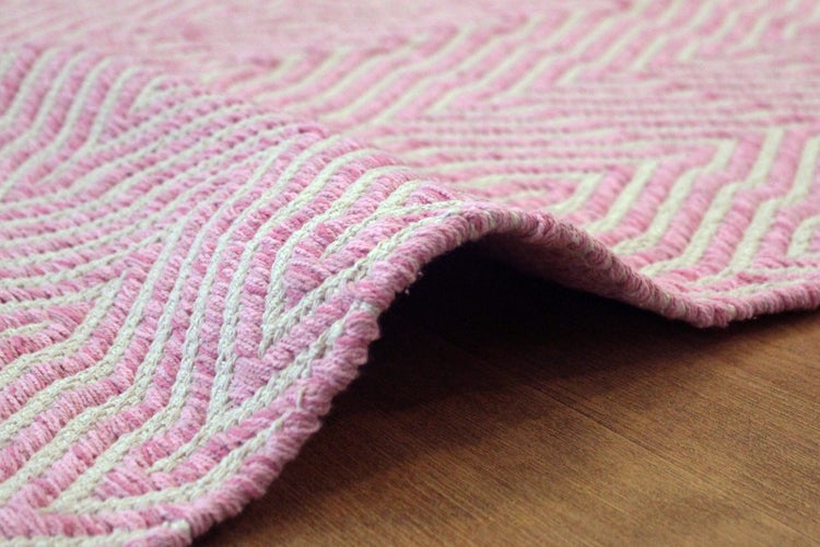 Nahaufnahme eines gewebten Teppichs mit rosa-weißem Zickzack-Muster aus Baumwolle auf Holzboden.