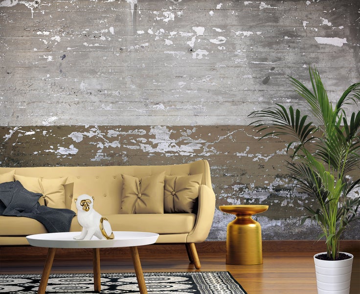 Vliestapete mit Motiv einer verwitterten Betonwand und abblätternder Farbe hinter einem gelben Sofa in einem modern eingerichteten Wohnzimmer.