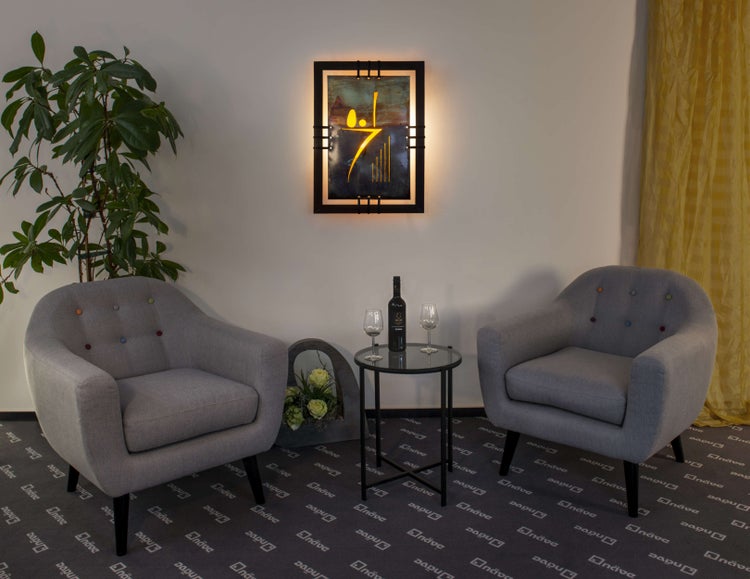 Zwei Sessel mit kleinem Tisch mit Wein und Gläsern, mit einer Pflanze und einem beleuchteten Kunstwerk an der Wand.