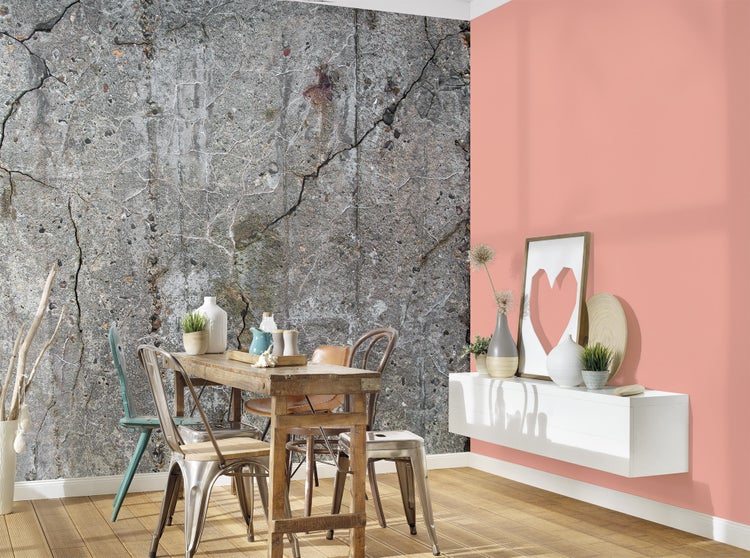 Fototapete in Betonoptik mit Rissen neben einer pfirsichfarbenen Wand, Esszimmer mit Holztisch und Metallstühlen.