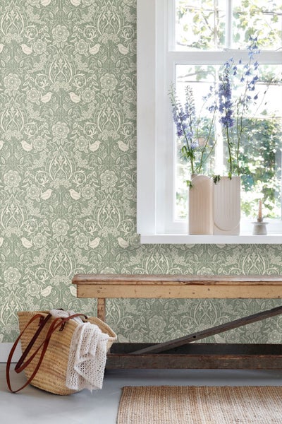 Tapete mit Blumenmuster und Vögeln in einem hellen Raum mit rustikaler Holzbank, Fenster und geflochtenem Korb.