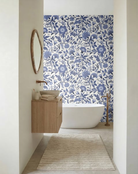 Modernes Badezimmer mit blau-weißer floraler Mustertapete, freistehender weißer Badewanne, Holz-Waschtisch mit Natursteinbecken und rundem Spiegel.