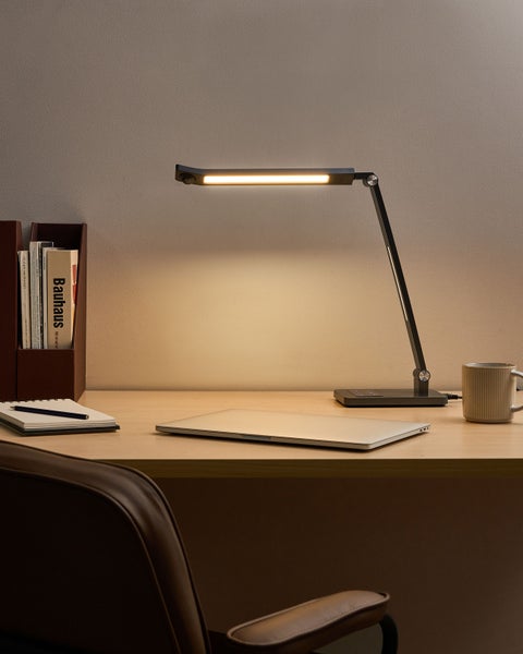 Schreibtisch mit Schreibtischlampe, Laptop, Notizbuch und Bücherregal für eine helle und organisierte Arbeitsumgebung.