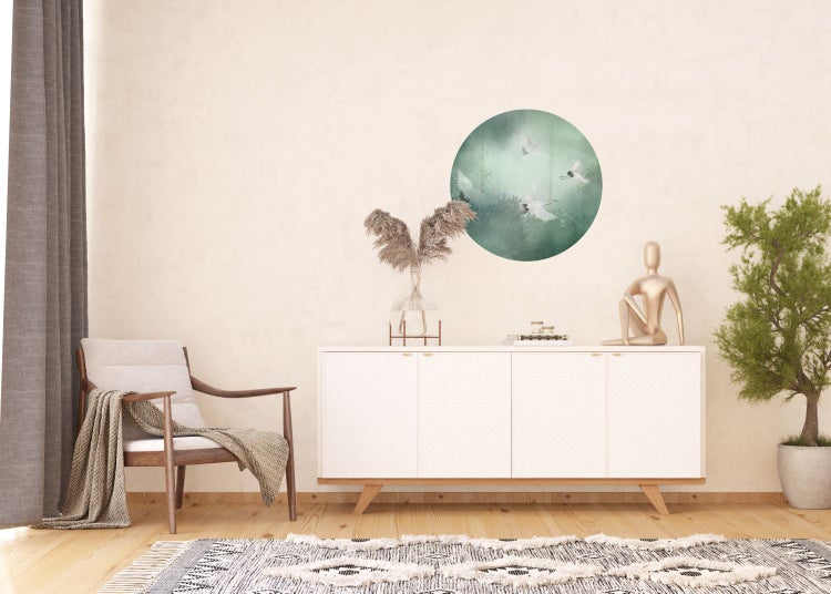 Innenraum mit weißem Sideboard, rundem Wandbild mit Kranichen und Dekorationen.