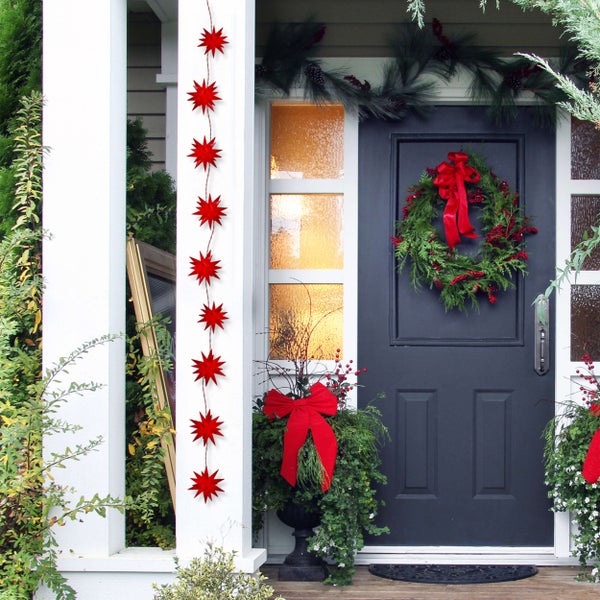 Dekorierte Haustür mit Sternengirlande, Kranz und Pflanzenarrangements für Weihnachten.