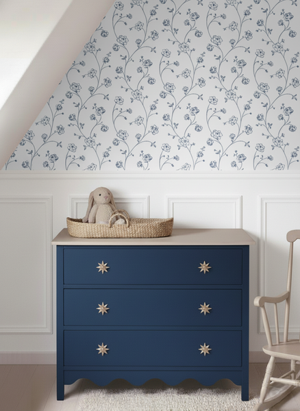 Vliestapete mit blauem Blumenmuster über weißer Wandtäfelung in einem Zimmer mit blauer Kommode und Schaukelstuhl.