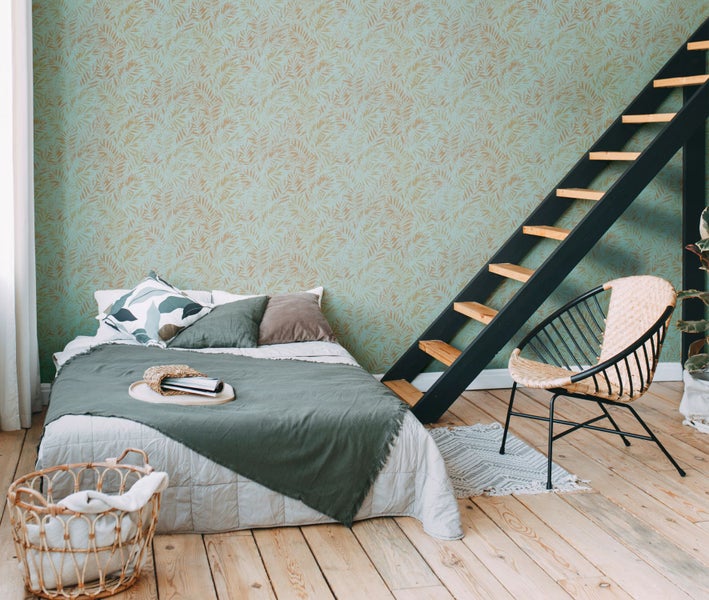 Helles Schlafzimmer mit Bett, Leiterregal, Rattansessel und gemusterter Tapete.