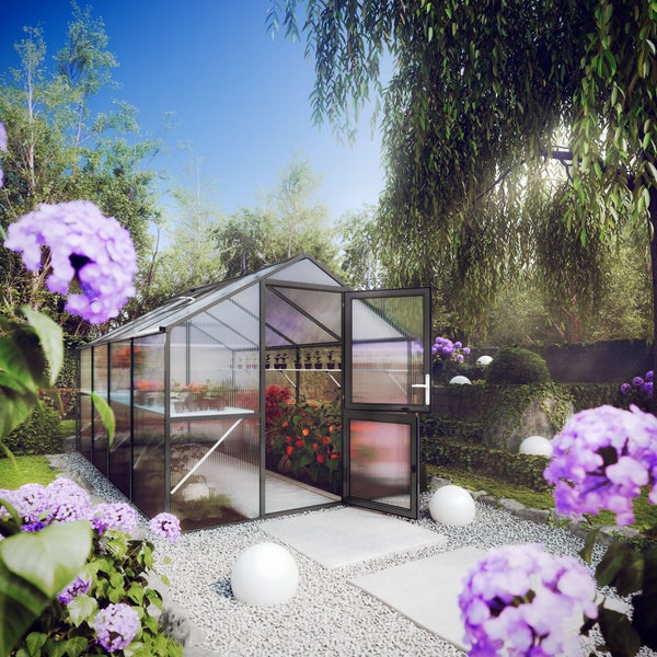 Modernes Gewächshaus mit dunklem Aluminiumrahmen und Hohlkammerplatten in einem hellen Garten mit Pflanzen und Kiesweg.