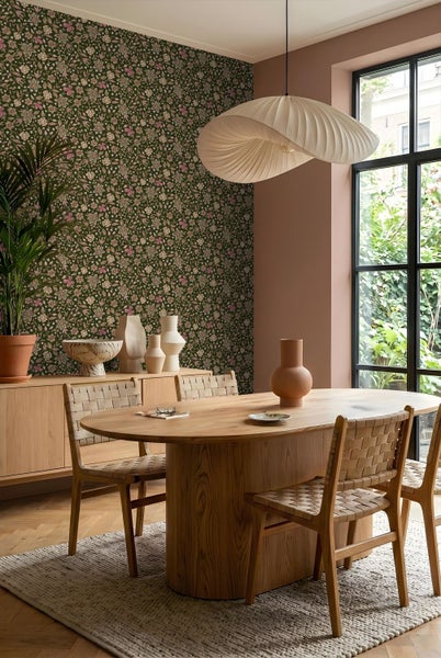 Helles Esszimmer mit ovalem Holztisch, geflochtenen Stühlen, floraler Mustertapete und einer großen wellenförmigen Pendelleuchte.