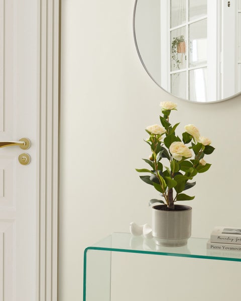 Dekorative Szene mit Kunstblumen in einem Topf auf einem Glastisch, einem runden Spiegel und einer Tür
