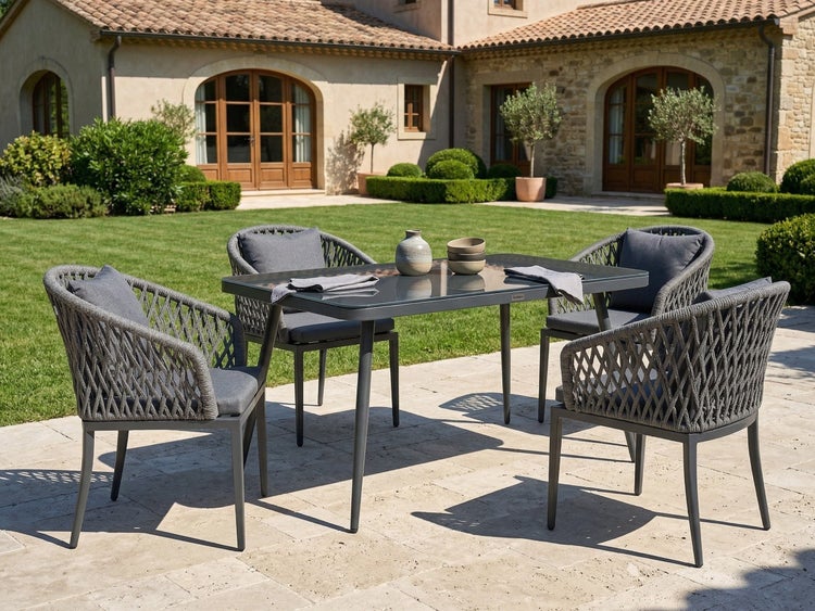 Gartenmöbel Set bestehend aus einem Esstisch mit Glasplatte und vier Stühlen mit Seilgeflecht Design auf einer Terrasse vor einem Landhaus.