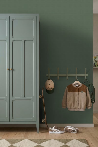 Organisierter Kinderbereich mit grünem Kleiderschrank, Wandgarderobe mit Kappe, Fleecejacke, Rucksack, Skateboard und Sneakers auf hellem Holzboden.