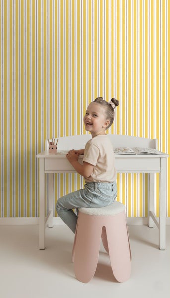 Ein Mädchen sitzt an einem Schreibtisch vor einer gelb gestreiften Tapete.