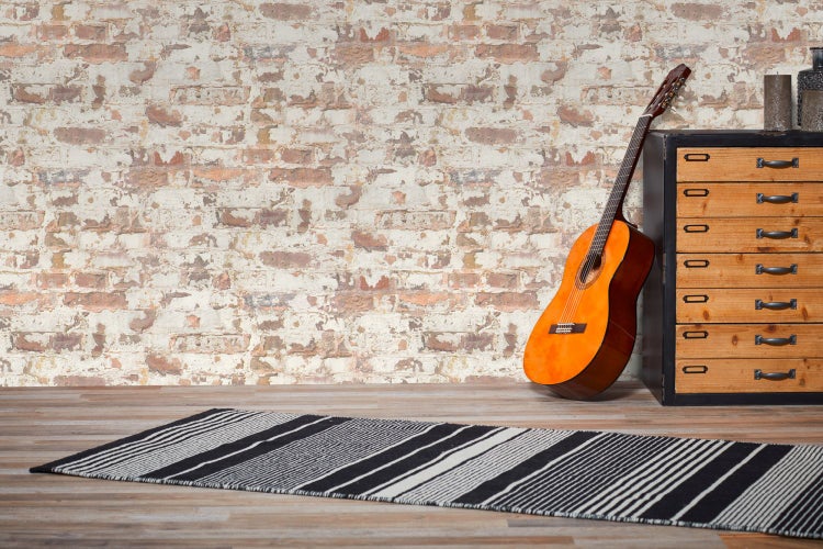 Mann mit lockigem Haar, Jeansjacke und Strickpullover vor einer Ziegelwand