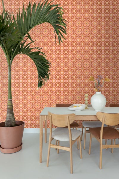 Helles Esszimmer mit Retromania Vliestapete mit floralem Retro-Muster, einem Holztisch, Stühlen und einer großen Zimmerpflanze.
