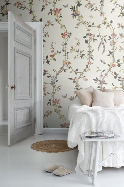 Helles Schlafzimmer mit floraler Tapete, Bett und offen stehender Tür