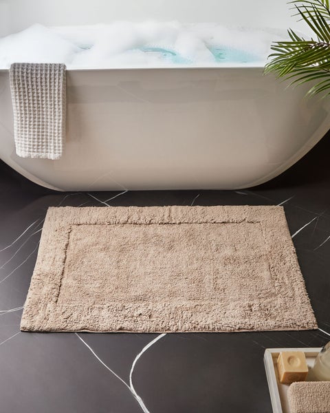 Beige Badematte vor einer Badewanne auf einem dunklen Marmorboden