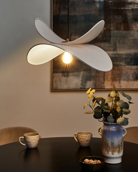 Szene mit einer modernen Pendelleuchte, einer Blumenvase und Geschirr auf einem Tisch.