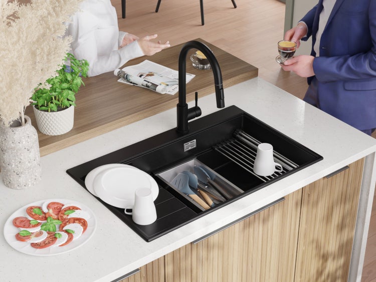 Schwarze Küchenspüle mit Abtropfgestell und Küchenutensilien auf einer Küchentheke.