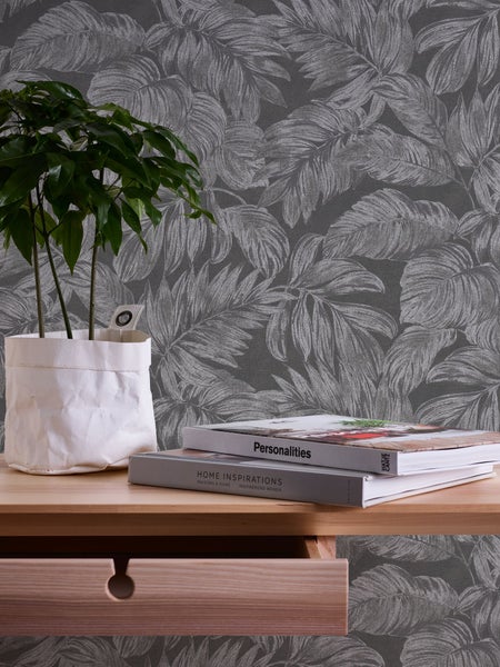 Dekorative Szene mit abstrakter Gesichtsskulptur, Zimmerpflanze, Stifthalter und Bleistift auf einem Tisch vor einer Tapete mit Blattmuster