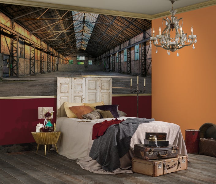 Fototapete mit Motiv einer Industriehalle in einem Schlafzimmer mit Vintage-Möbeln, Bett mit Holzkopfteil und Kronleuchter.
