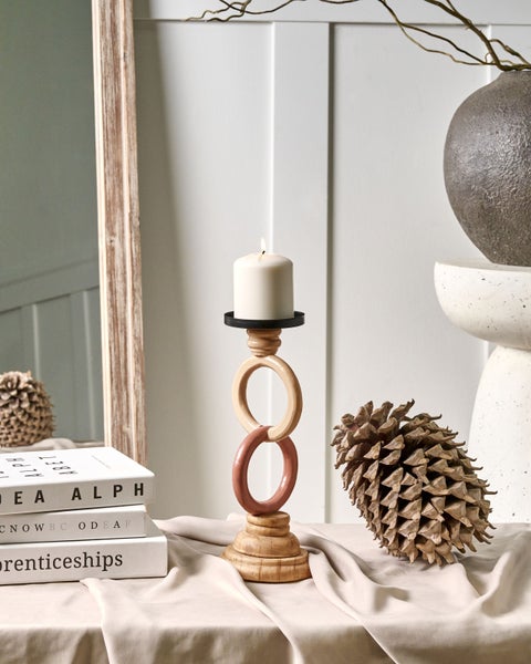 Dekoratives Stillleben mit Kerzenständer, Kerze, Büchern und großem Tannenzapfen