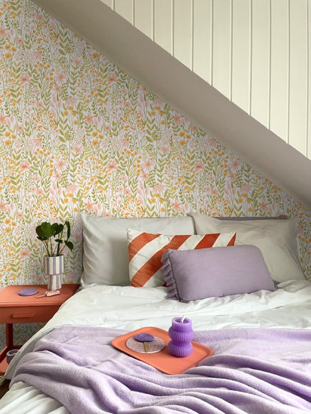 Schlafzimmer mit floraler Tapete, Bett, Nachttisch und dekorativen Elementen für eine gemütliche Atmosphäre.