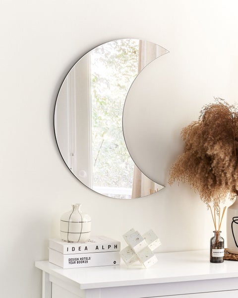 Dekorativer Spiegel in Halbmondform über einem weißen Beistelltisch mit Vasen und Dekoration