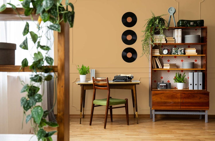 Vintage-Arbeitszimmer mit Holzschreibtisch, Schreibmaschine, Holzstuhl und großem Bücherregal vor einer ockerfarbenen Wand mit Zierleisten.