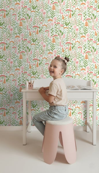 Mädchen am Schreibtisch vor einer Wand mit Blumenmuster-Tapete