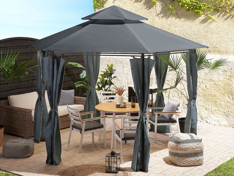 Gartenpavillon mit grauem Dach und Vorhängen, auf einer Terrasse mit Holztisch, weißen Stühlen und einem Sofa aus Polyrattan.