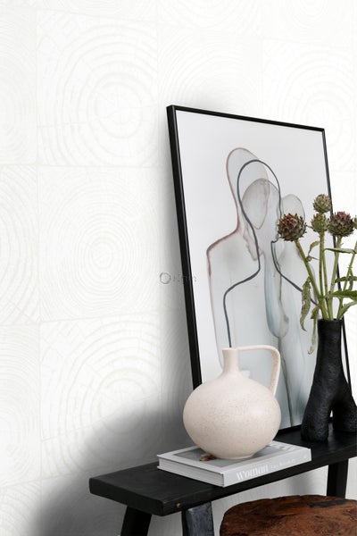 Dekorative Szene mit einer Wandtapete mit Baumringmuster, einem gerahmten Bild, einer Vase mit Blumen und einer Keramikkanne auf einem schwarzen Regal.