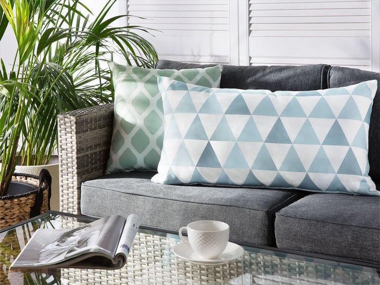 Gartenmöbel mit Zierkissen, Zeitschrift und Kaffeetasse auf dem Tisch