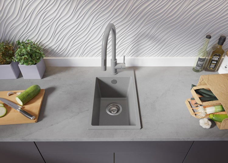 Küchenszene mit Spüle, Armatur, Schneidebrett, Gemüse und dekorativen Elementen auf einer Arbeitsplatte.