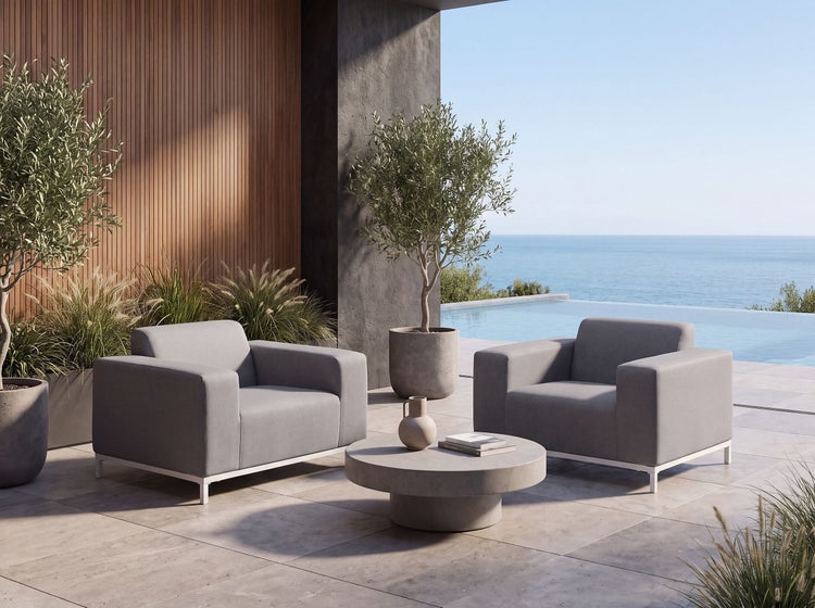 Moderne Loungegruppe mit zwei Sesseln und rundem Betontisch auf einer Terrasse mit Pool und Meerblick.