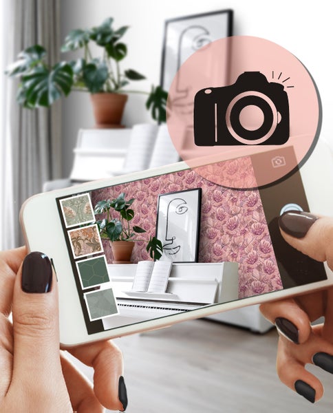 Person hält ein Smartphone mit einer App zur Visualisierung von Tapeten in einem Raum.