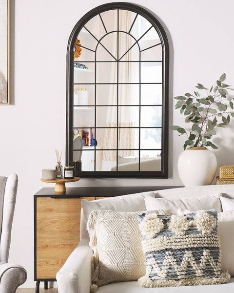 Dekorative Wohnszene mit einem schwarzen Bogenfensterspiegel, einem Sideboard, Kissen und Dekorationsgegenständen.